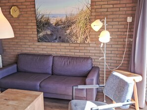 A modern living room with a brick wall, a sofa, a chair, a lamp, and a clock. - De Blenck 66 by Interhome (Callantsoog)