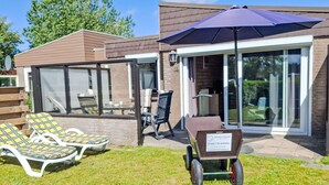 A modern outdoor area with a patio, lounge chairs, a table, and a wheelbarrow. - De Blenck 66 by Interhome (Callantsoog)