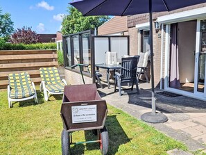 A patio area with outdoor furniture, a wheelbarrow, and a sliding glass door leading to a covered outdoor space. - De Blenck 66 by Interhome (Callantsoog)