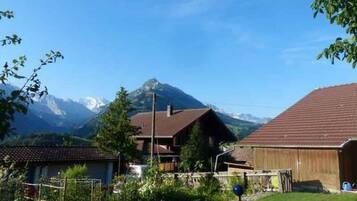 Une maison de campagne aux murs en bois, entourée d’un jardin et adossée à une montagne.