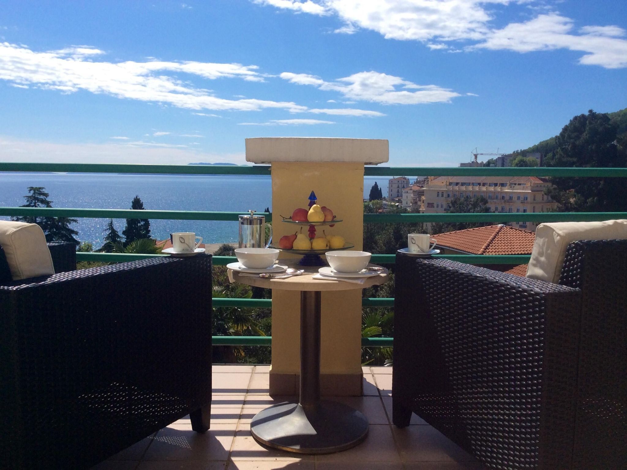 Una terraza con sillones de mimbre, una mesa con frutero y vista al mar.