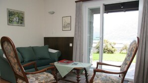 En stue med en grøn sofa, to træstole med blomstret betræk, et lille bord med en bog og en gulvtæppe med et mønster.