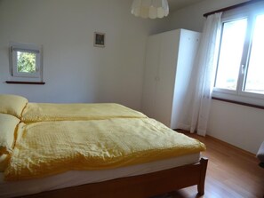 Un dormitorio con cama, armario, ventana y un pequeño cuadro en la pared.