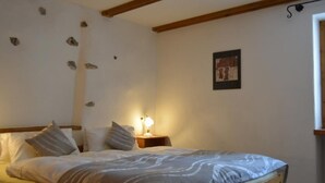 A bedroom with a bed, wooden headboard, a nightstand with a lamp, and a wall with decorative stones. - Bos-cha by Interhome (La Punt-Chamues-ch)