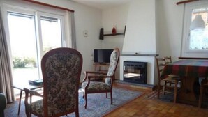 Een woonkamer met een open haard, een televisie en een eethoek met een tafel en stoelen.