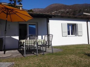Ein weißes Gebäude mit einer Terrasse, einem Tisch mit Stühlen und einem Sonnenschirm.
