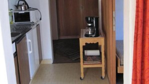 Un pasillo estrecho con una zona de cocina a la izquierda, una puerta de madera al fondo y una pequeña mesa con una cafetera en el centro.