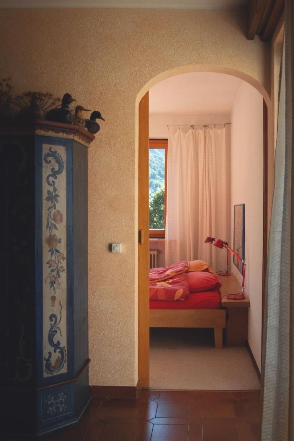 Un dormitorio con cama, mesita de noche, lámpara y ventana con cortinas.