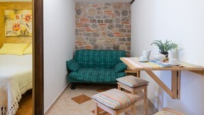 Una habitación acogedora con un sofá verde, una mesita de madera con una planta y una cama con un cojín amarillo.