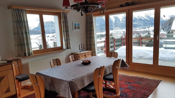 Ein Esszimmer mit einem Tisch für sechs Personen, großen Fenstern mit Blick auf schneebedeckte Berge und einer Kristallleuchter.