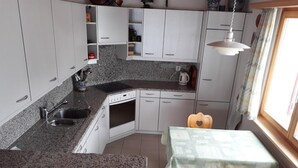 Eine kompakte Küche mit weißen Schränken, einer Arbeitsplatte aus Granit, einem Einbauofen und einem Essbereich mit Tisch und Stühlen.