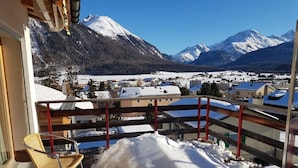 Ein Balkon mit Korbstühlen, verschneiter Boden und Blick auf eine Stadt und Berge.