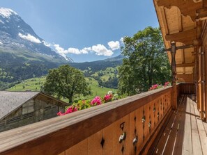 Ein hölzerner Balkon mit Blick auf eine gebirgige Landschaft, darunter ein markanter Gipfel und üppige, grüne Täler.