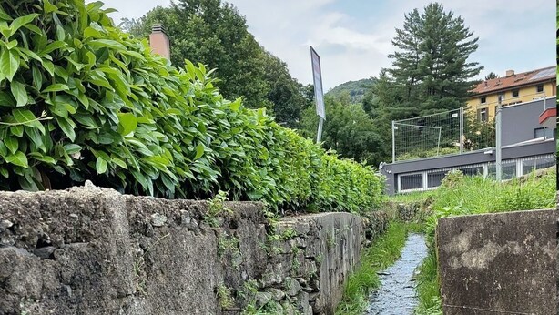 Een smalle stenen goot met stromend water, omzoomd door stenen muren en groene begroeiing.