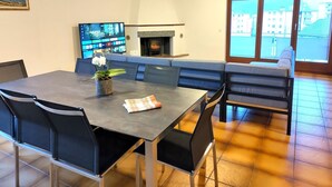 Een eetgedeelte met een tafel, stoelen, een bank, een open haard en een televisie.
