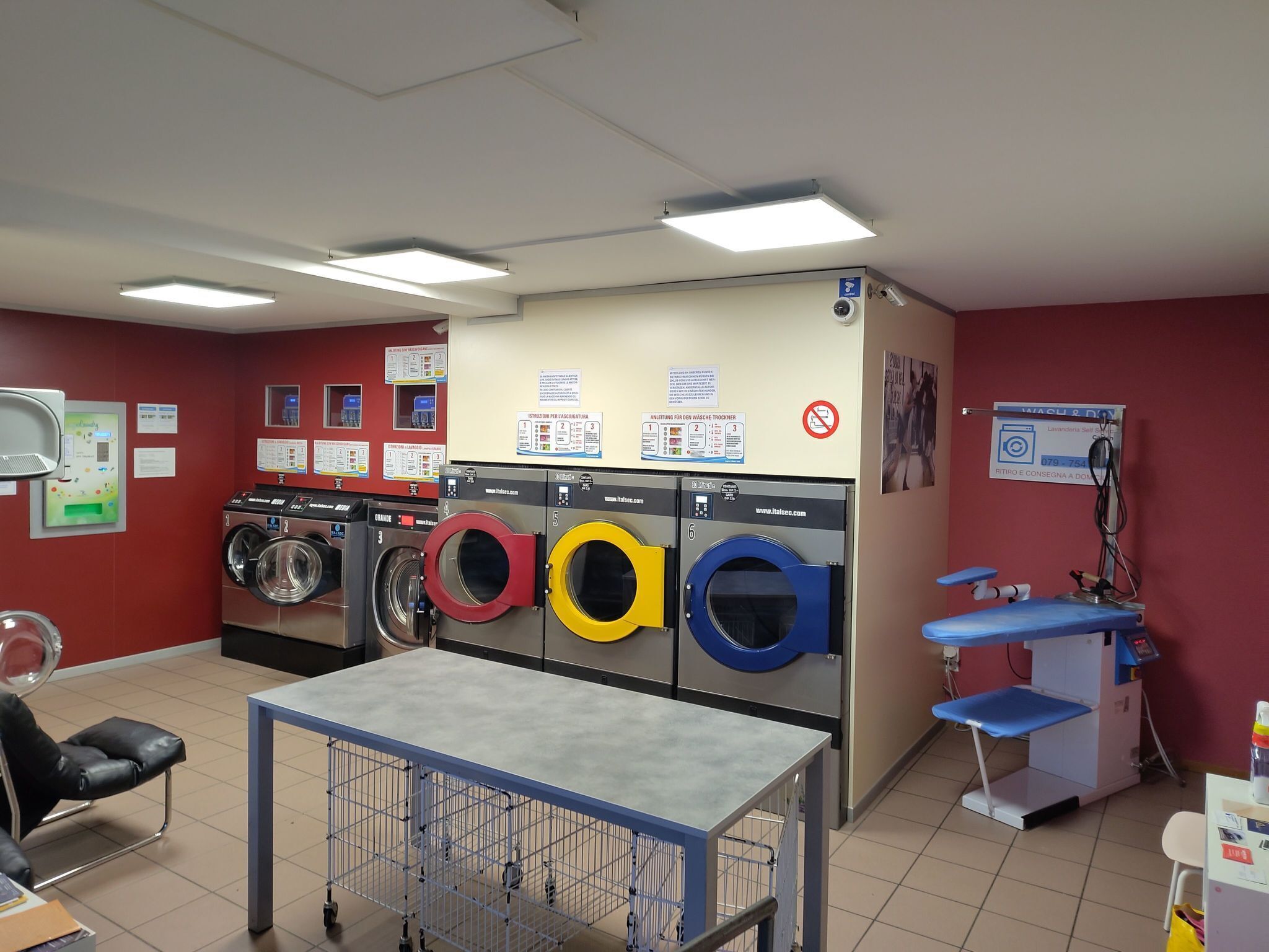 Une buanderie équipée de plusieurs machines à laver, une table avec un cadre en métal et un banc bleu.