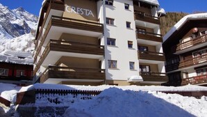 Un hotel pluripiano chiamato CRESTA, con tetto e balconi imbiancati dalla neve, sullo sfondo di montagne.