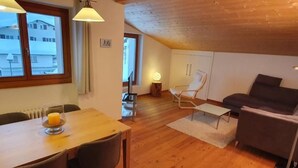 Un salon chaleureux avec un plafond en bois, un canapé, une table à manger avec des chaises et une vue sur l’extérieur par une fenêtre.