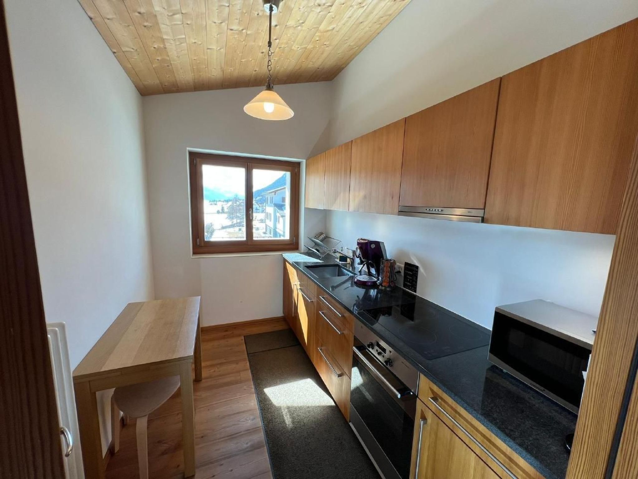 A compact kitchen with wooden cabinets, a black countertop, and a window offering a view.