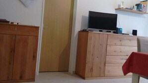 Ein Zimmer mit einem Holzschrank, einem Fernseher auf einem Standfuß, einer geschlossenen Tür und einem Bücherregal.