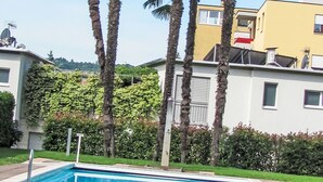 Ein Wohngebäude mit Swimmingpool, Palmen und einer grünen Hecke.