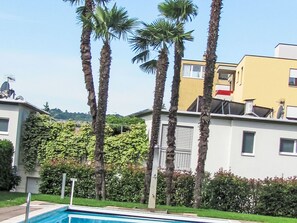 Edificio residencial con piscina, palmeras y seto verde.