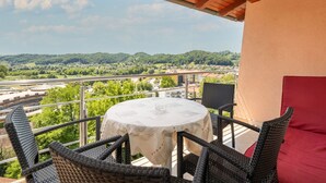Un balcone con sedie in vimini e un tavolo, affacciato su un panorama suggestivo con colline e una strada.