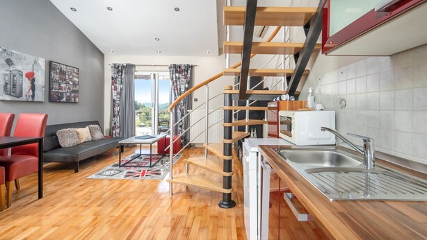 Un appartamento moderno con una scala in legno, una cucina con lavandino, un'area pranzo con sedie rosse e un soggiorno con divano e tavolo.