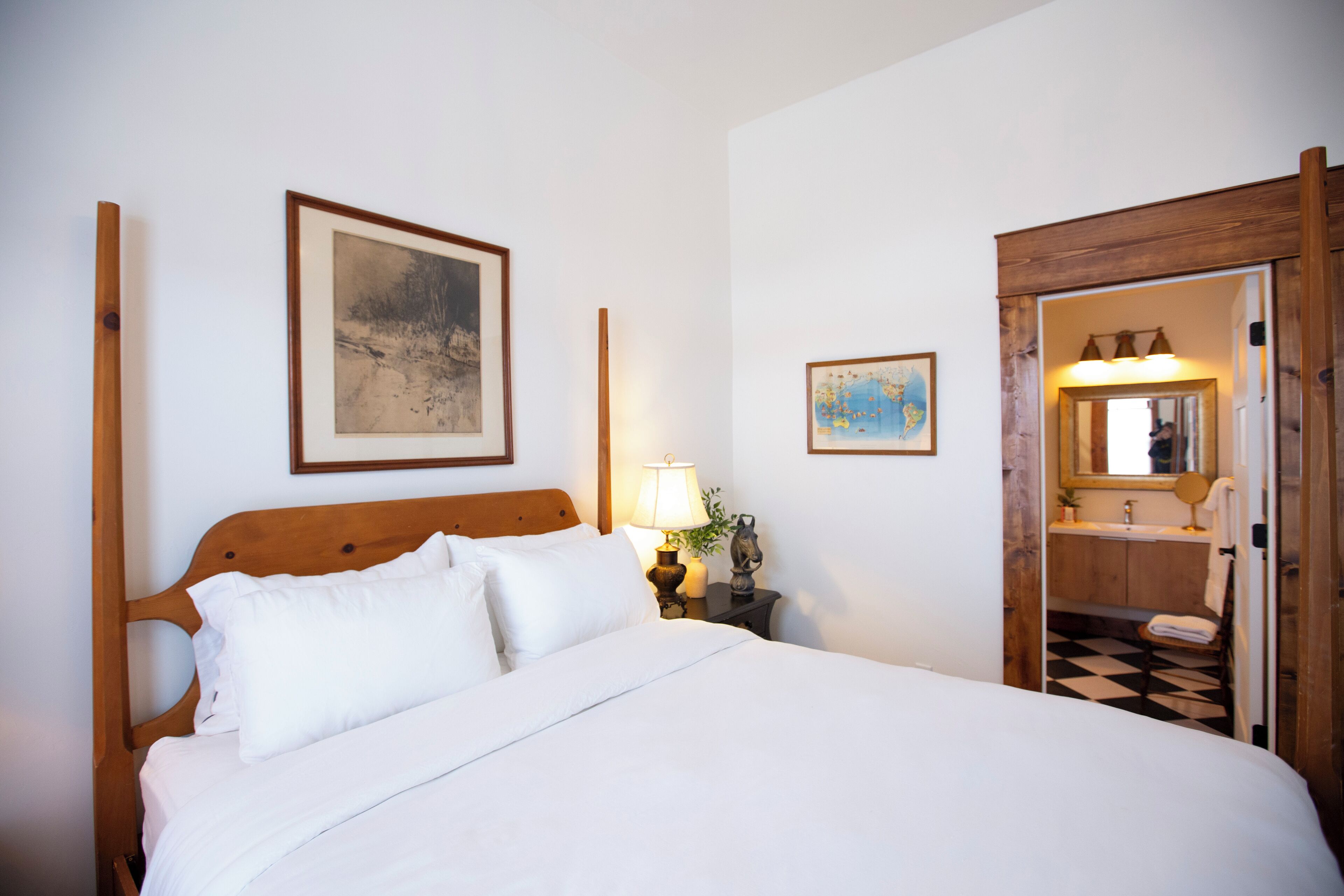 A neatly made bed with white linens, a wooden headboard, and a nightstand with a lamp and a small decorative item.