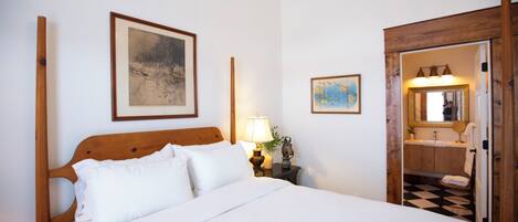 A neatly made bed with white linens, a wooden headboard, and a nightstand with a lamp and a small decorative item.