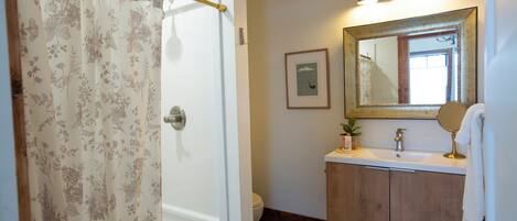 A bathroom with a checkered floor, a wooden cabinet, a sink with a mirror, and a shower curtain with floral patterns.
