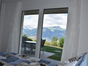 Een slaapkamer met een bed, een tafel, stoelen en een schuifdeur die uitkomt op een balkon met uitzicht op de bergen.