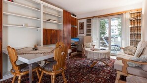 Una sala de estar con una mesa de comedor, sillas, un sofá, una estantería y vistas al exterior.