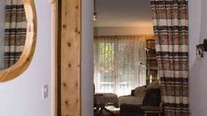 Un pasillo estrecho con una cama, una escalera de madera, un espejo circular y una cortina de cuadros.