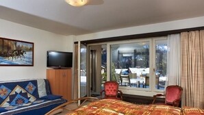 Ein Schlafzimmer mit einem großen Bett, einer Couch, einem Fernseher und Blick ins Freie durch eine Schiebetür.