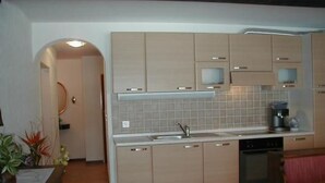 Eine kleine Küche mit hellen Holzschränken, einem eingebauten Backofen und einer Kaffeemaschine auf der Arbeitsplatte.