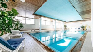 An indoor swimming pool with clear blue water, surrounded by white lounge chairs and potted plants. - Holiday Park A06 by Interhome (St. Moritz)