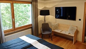 A bedroom with a bed, a chair, a sofa, a TV, and a window with a view of trees. - Holiday Park A06 by Interhome (St. Moritz)
