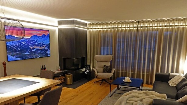 A modern living room with a wooden dining table, a sofa, a TV, and a fireplace. - Holiday Park A06 by Interhome (St. Moritz)