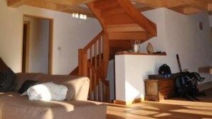A spacious loft with high ceilings, exposed wooden beams, and a large window allowing natural light. A sofa is positioned near a doorway, and a small table with items is visible in the background. - Blue Merle by Interhome (Vercorin)