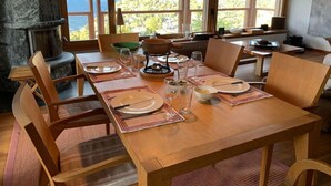 A dining area with a table set for four, a stone fireplace, and a view of mountains through large windows. - Blue Merle by Interhome (Vercorin)