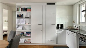 Een moderne keuken met witte kasten, een inbouwboekenplank en een eethoek met een tafel en stoelen.