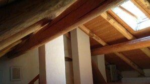 Quarto no sótão com vigas de madeira aparentes, claraboia e teto inclinado.