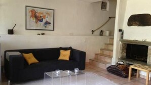 Uma sala de estar com um sofá preto, uma lareira, uma escada e um quadro na parede.