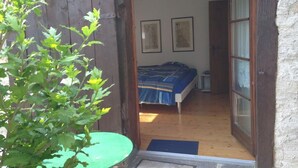 Um quarto com uma cama, uma mesa pequena e uma porta que dá para outro aposento.