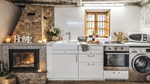 A kitchen with white cabinets, a stone fireplace, a microwave, and a washing machine.
