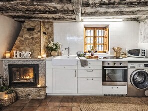 A kitchen with white cabinets, a stone fireplace, a microwave, and a washing machine.