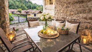 A table set with candles, flowers, and a wicker basket in a stone-walled outdoor area with a view of greenery.