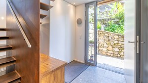 Un interior moderno con una escalera de madera, un vidrio que da al exterior y una pared de piedra visible a través del vidrio.