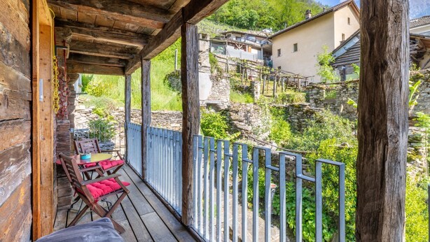 Un porche de madera con una mesa y sillas, con vistas a una zona montañosa con edificios de piedra.